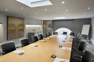 Ein Konferenzraum mit einem langen Tisch, Stühlen, einer Tafel und einem großen, abstrakten Gemälde an der Wand.