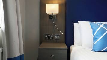 A hotel room with a bed, a nightstand with a lamp, and a wall socket.