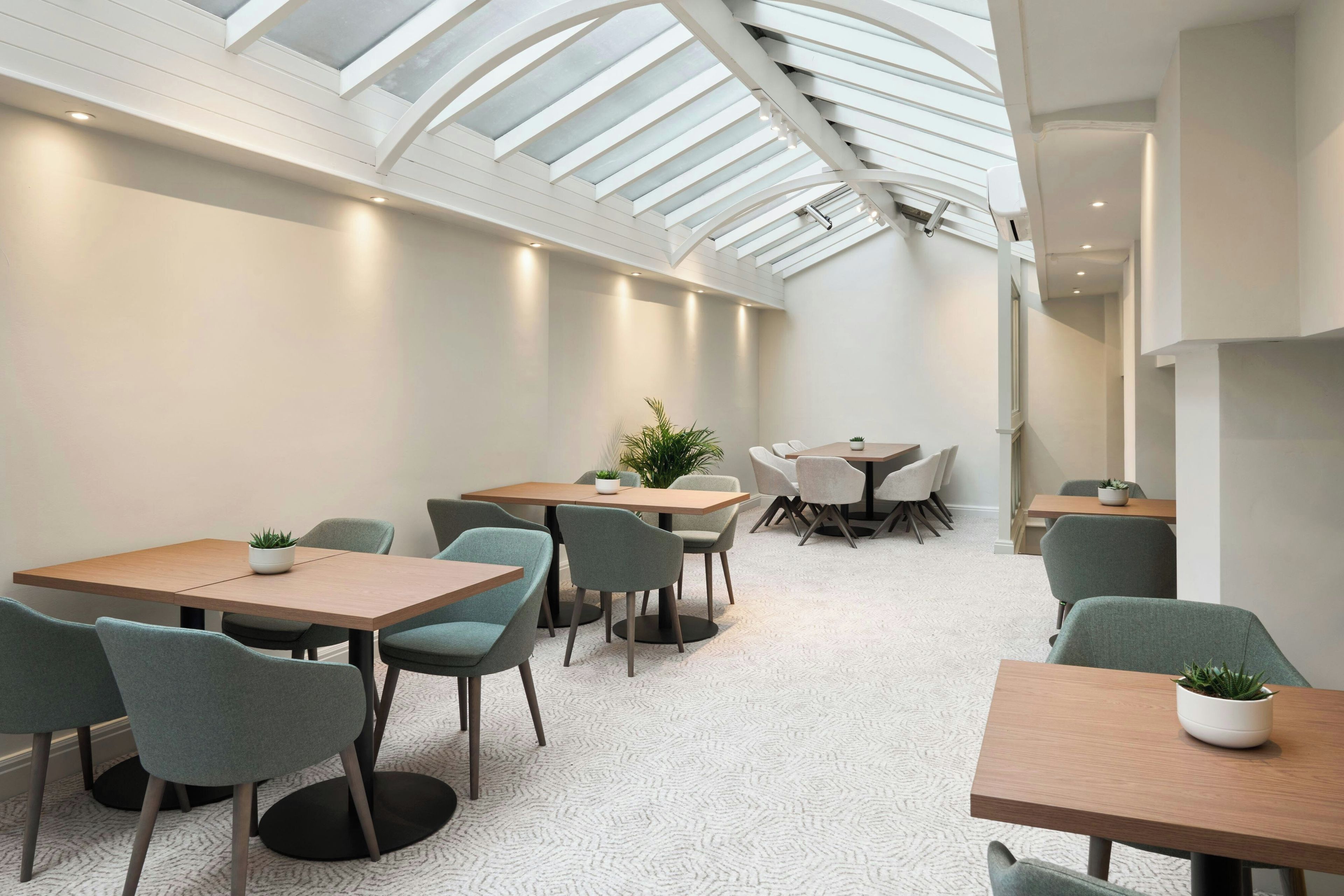 A modern interior with a high ceiling and skylight, featuring multiple tables and chairs arranged for dining or meetings.