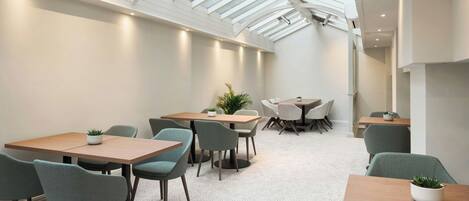 A modern interior with a high ceiling and skylight, featuring multiple tables and chairs arranged for dining or meetings.