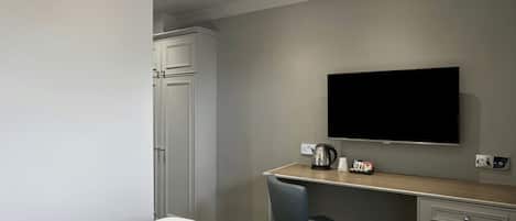 A hotel room with a bed, a desk with a chair, a television, and a wardrobe.