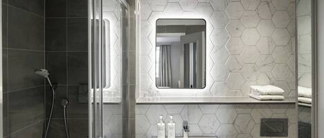 A modern bathroom with a glass shower enclosure, a sink with a mirror above, and hexagonal marble tiles.