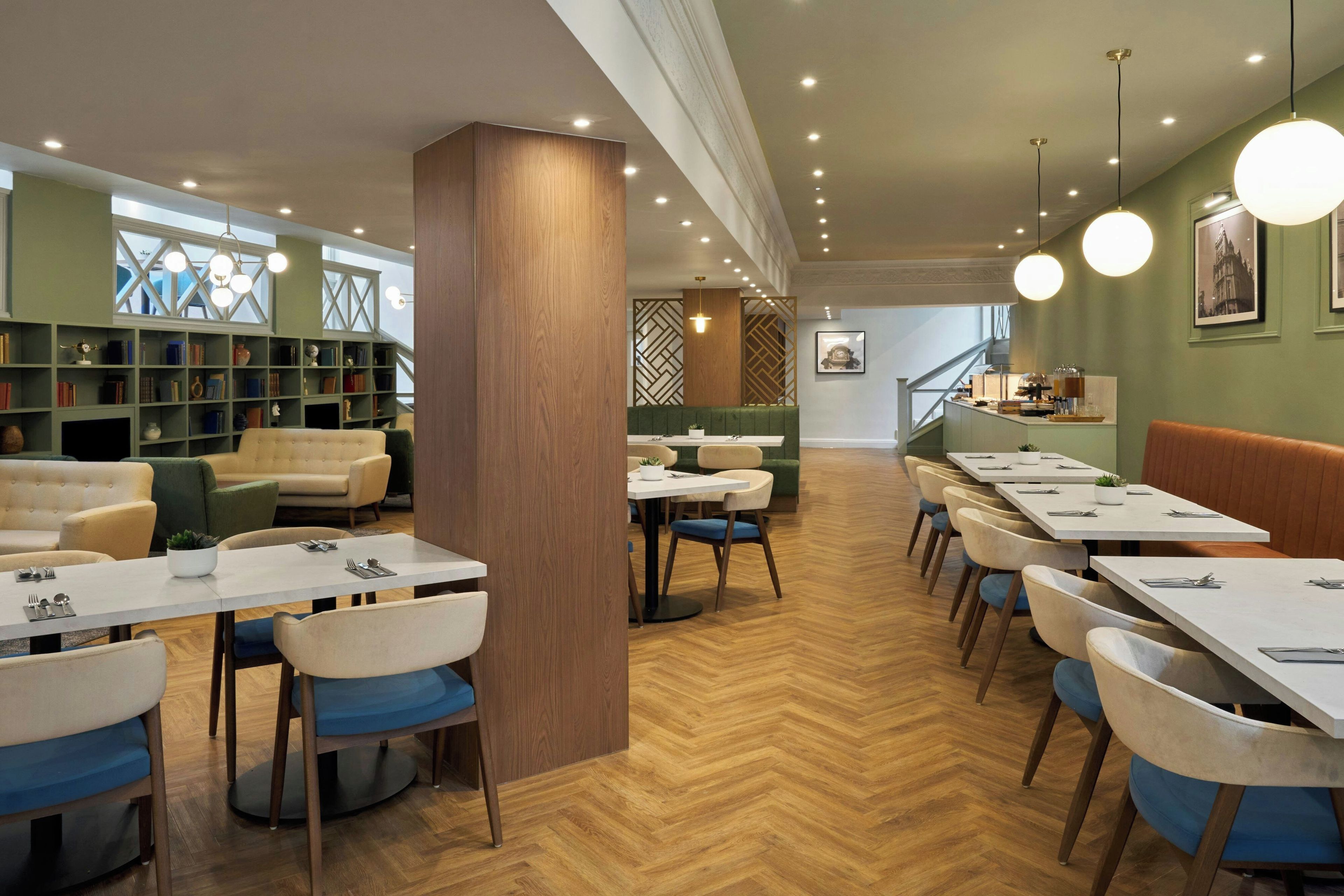 A restaurant with multiple dining tables and chairs, a bookshelf, and a staircase leading to an upper level.
