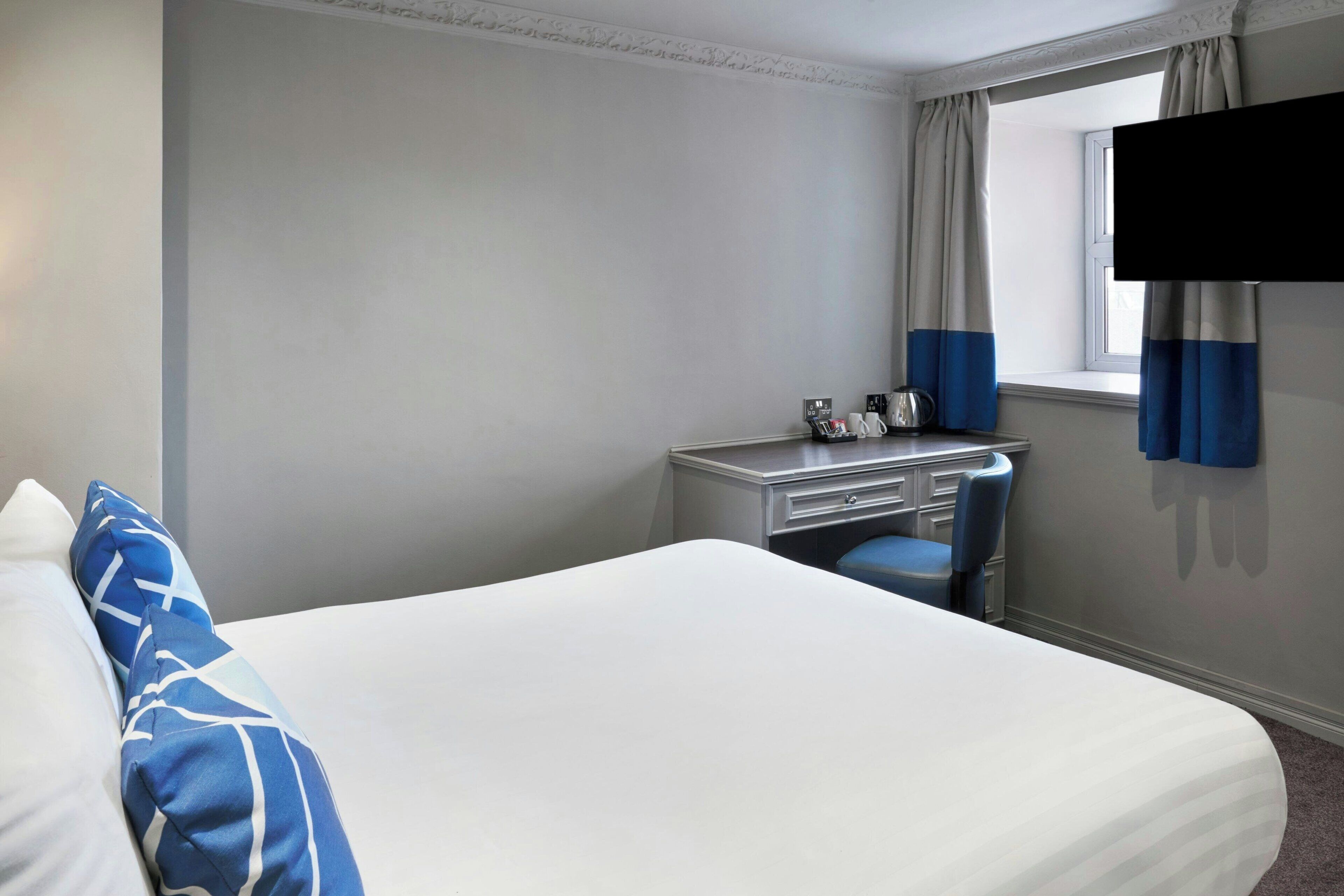 A hotel room with a bed, a desk, a chair, and a window with curtains.