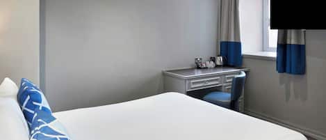 A hotel room with a bed, a desk, a chair, and a window with curtains.