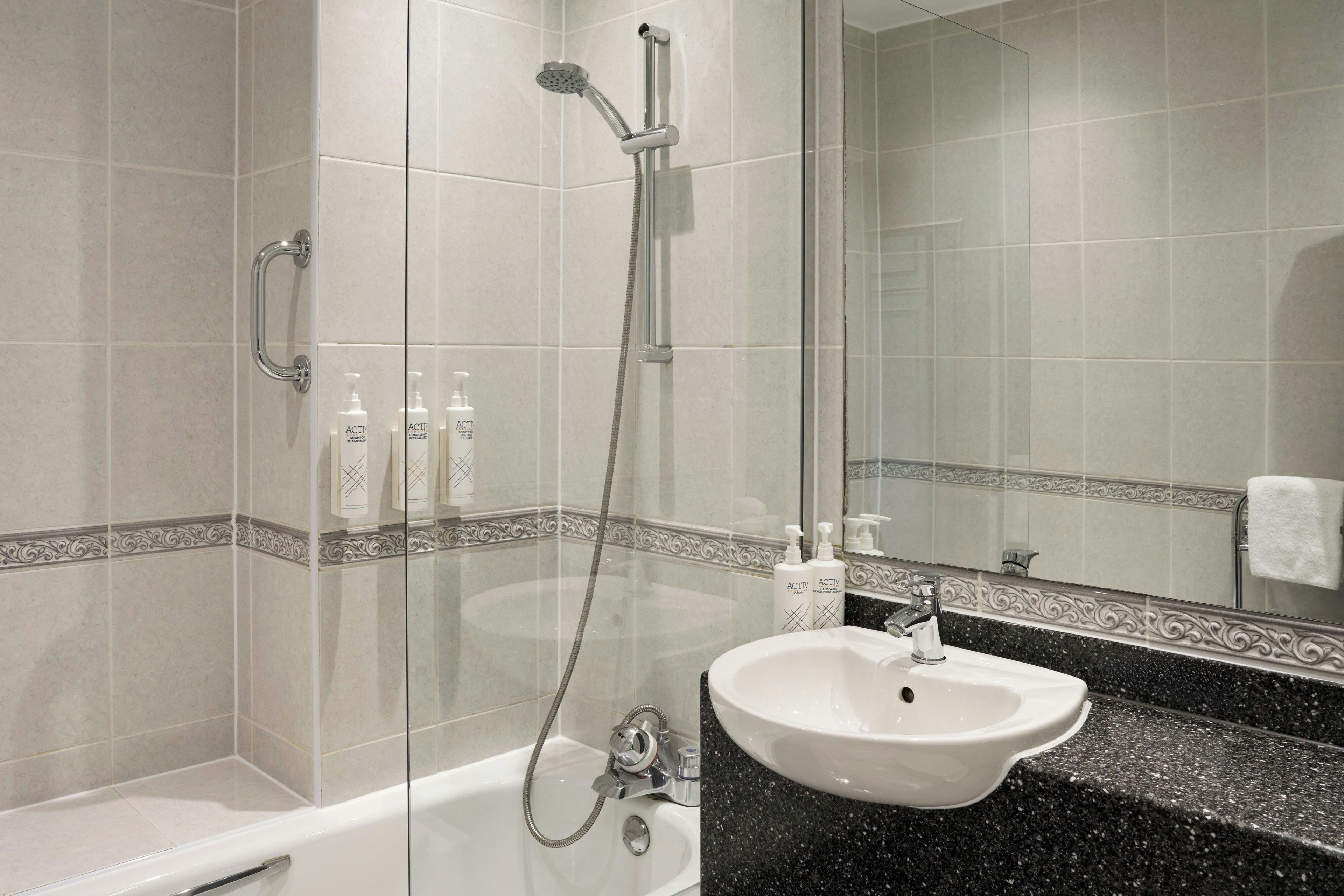 A bathroom with a bathtub, a sink, and a shower. There are bottles of shampoo and conditioner on the counter.
