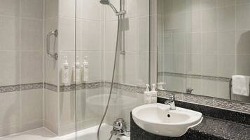 A bathroom with a bathtub, a sink, and a shower. There are bottles of shampoo and conditioner on the counter.