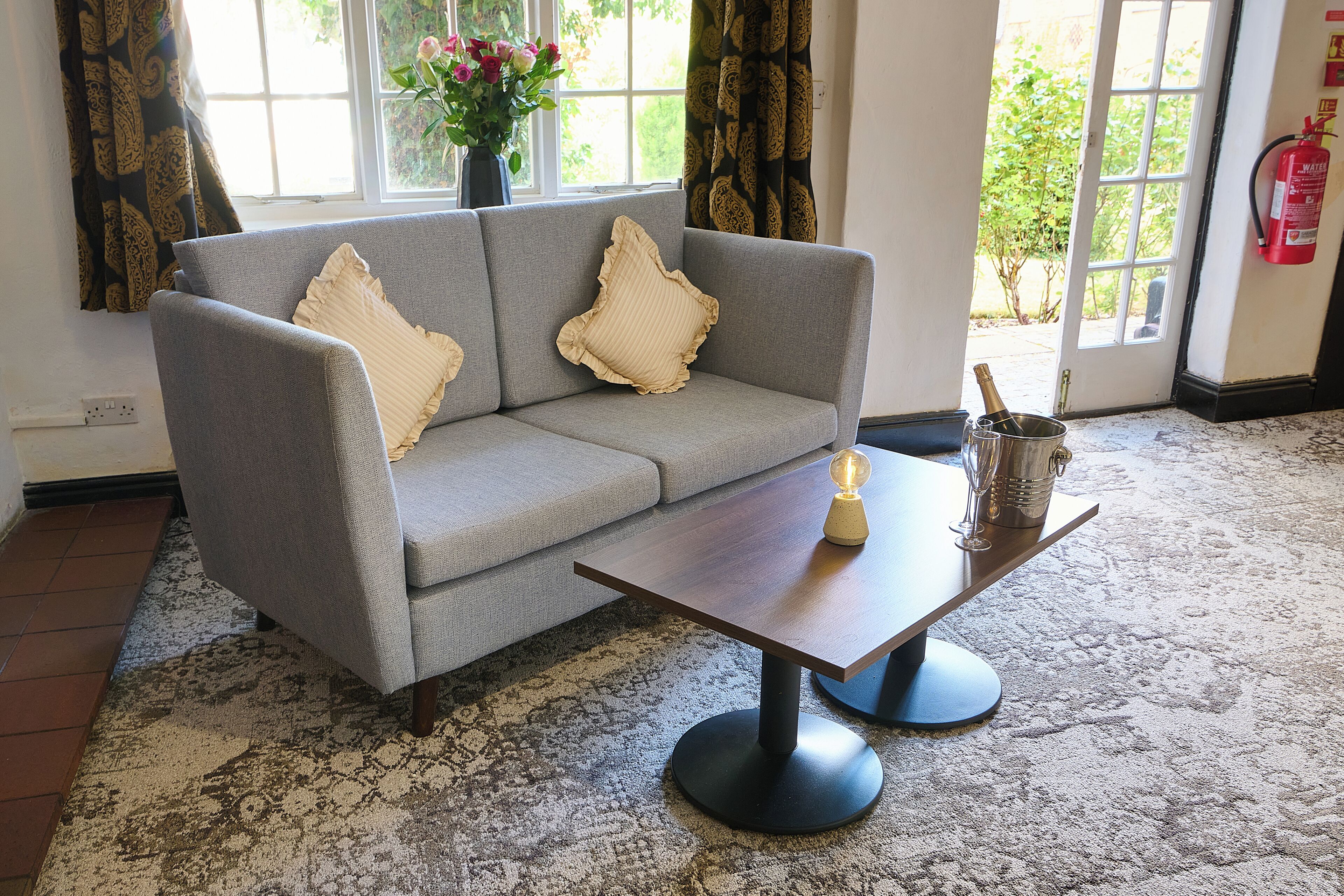 A grey sofa with ruffled pillows, a wooden coffee table, and a vase with flowers.