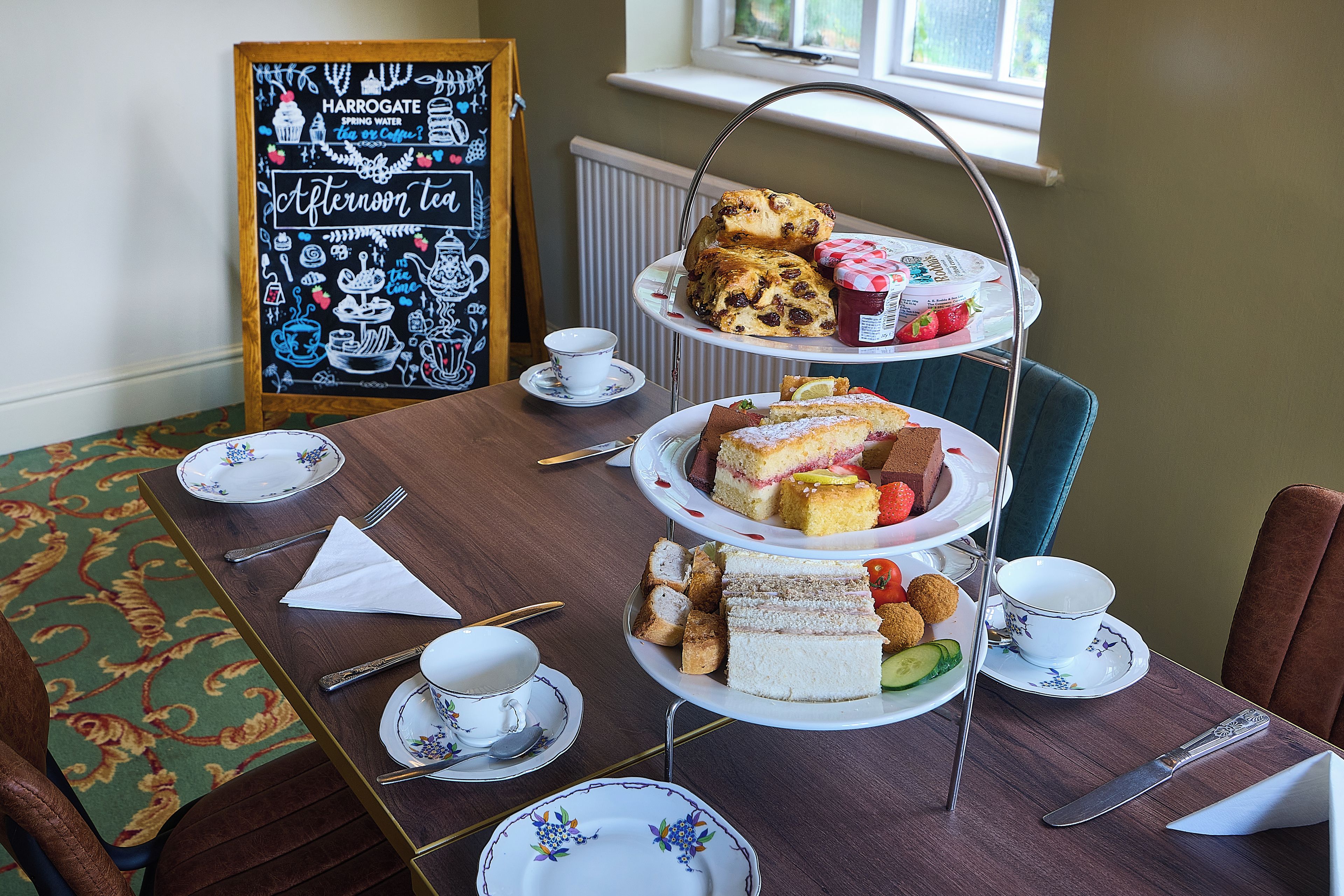 A three-tiered tea service set on a table with a chalkboard in the background.
