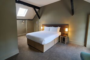 A hotel room with a large bed, a nightstand with a lamp, a wooden headboard, and a skylight. - Marston Farm Hotel (Sutton Coldfield)