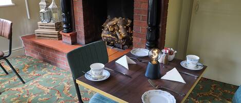A dining area with a brick fireplace, a table set for two, and a patterned carpet.