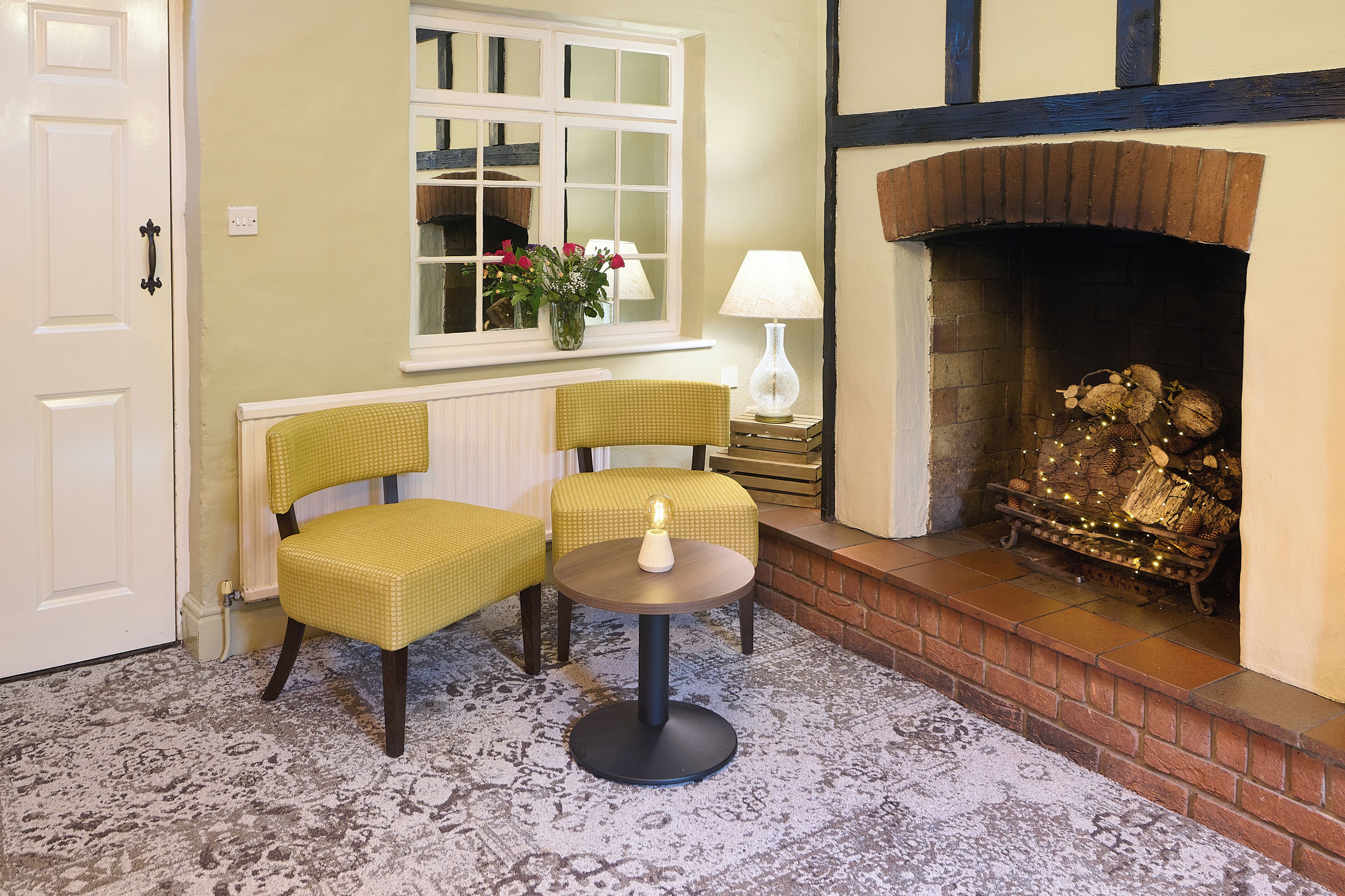 A cozy room with a fireplace, two chairs, a small table, and a window with a view.