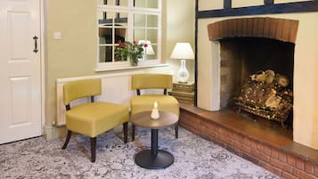 A cozy room with a fireplace, two chairs, a small table, and a window with a view.