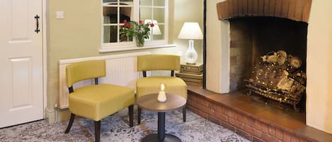 A cozy room with a fireplace, two chairs, a small table, and a window with a view.