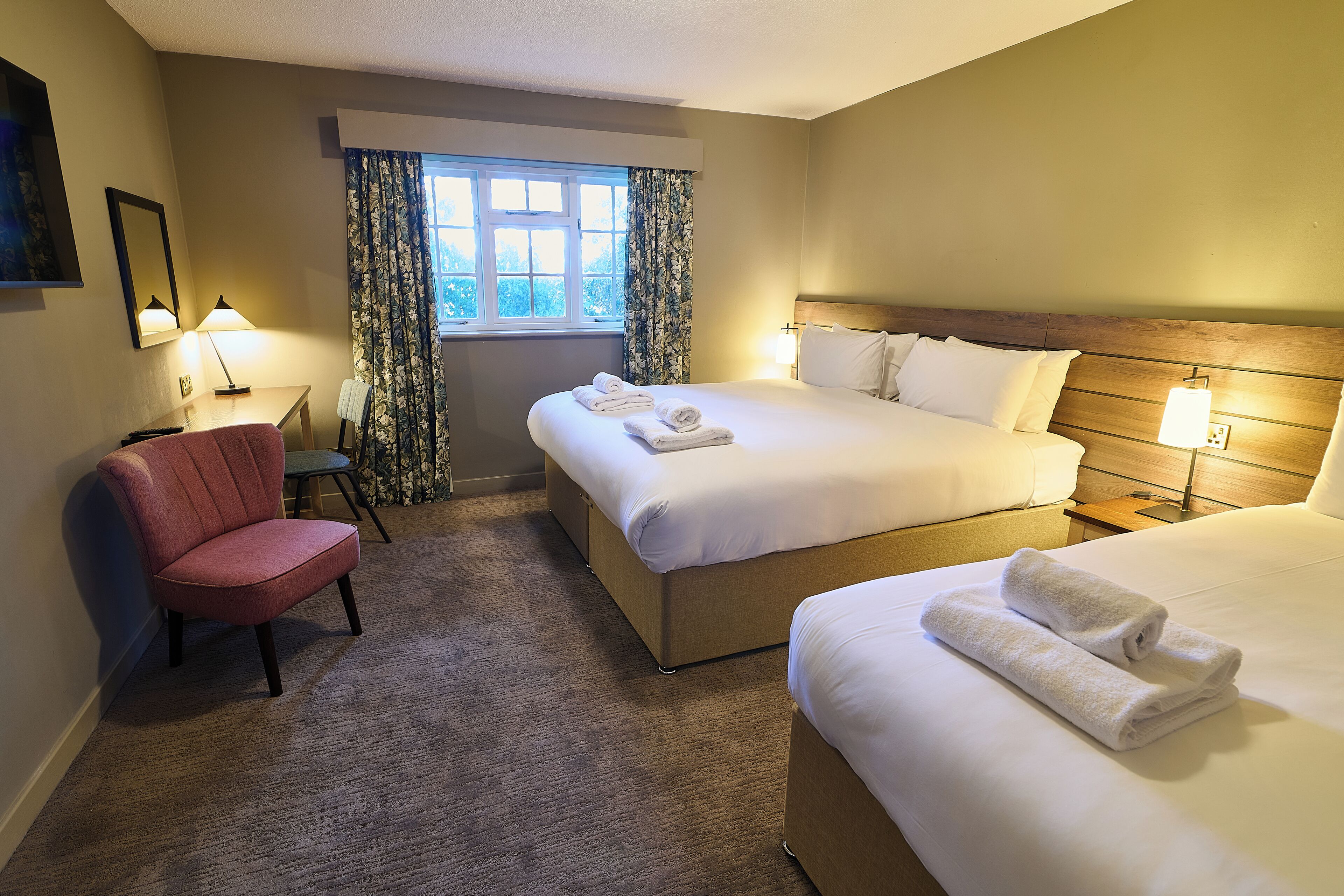 A hotel room with a bed, a chair, a desk, and a window with curtains.