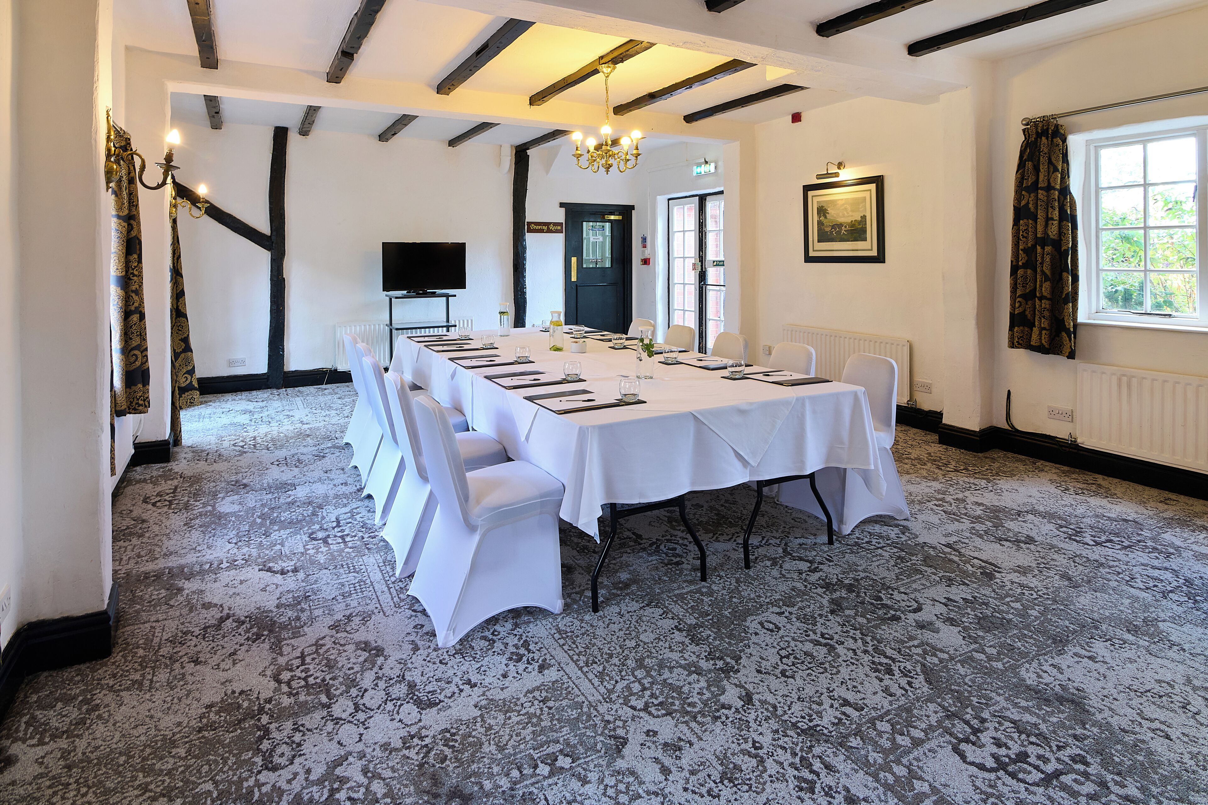 A conference room with a long table, white chairs, a chandelier, and a large window with curtains.