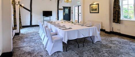 A conference room with a long table, white chairs, a chandelier, and a large window with curtains.