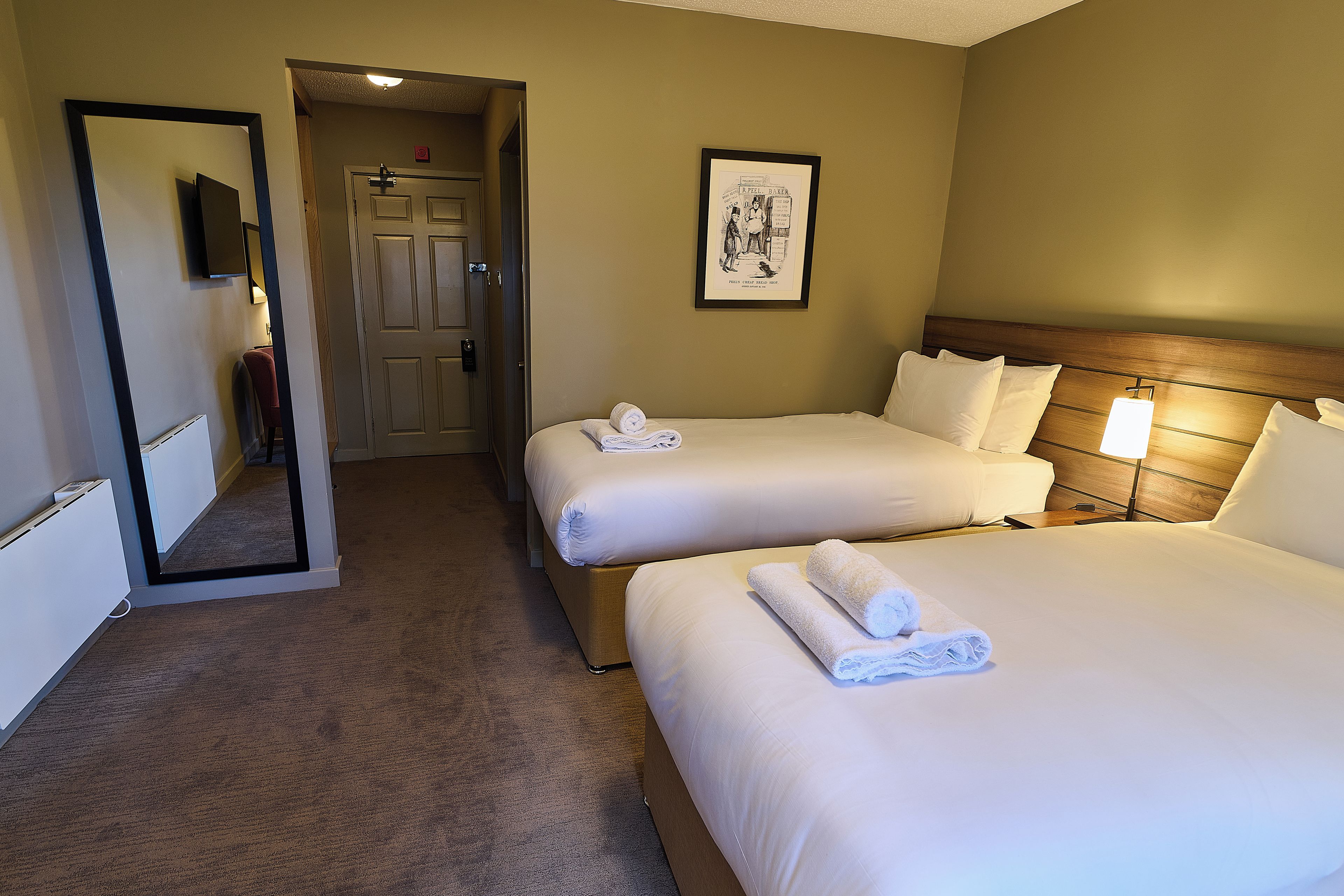 A hotel room with two beds, a door, a framed picture on the wall, and a carpeted floor.