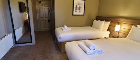 A hotel room with two beds, a door, a framed picture on the wall, and a carpeted floor.