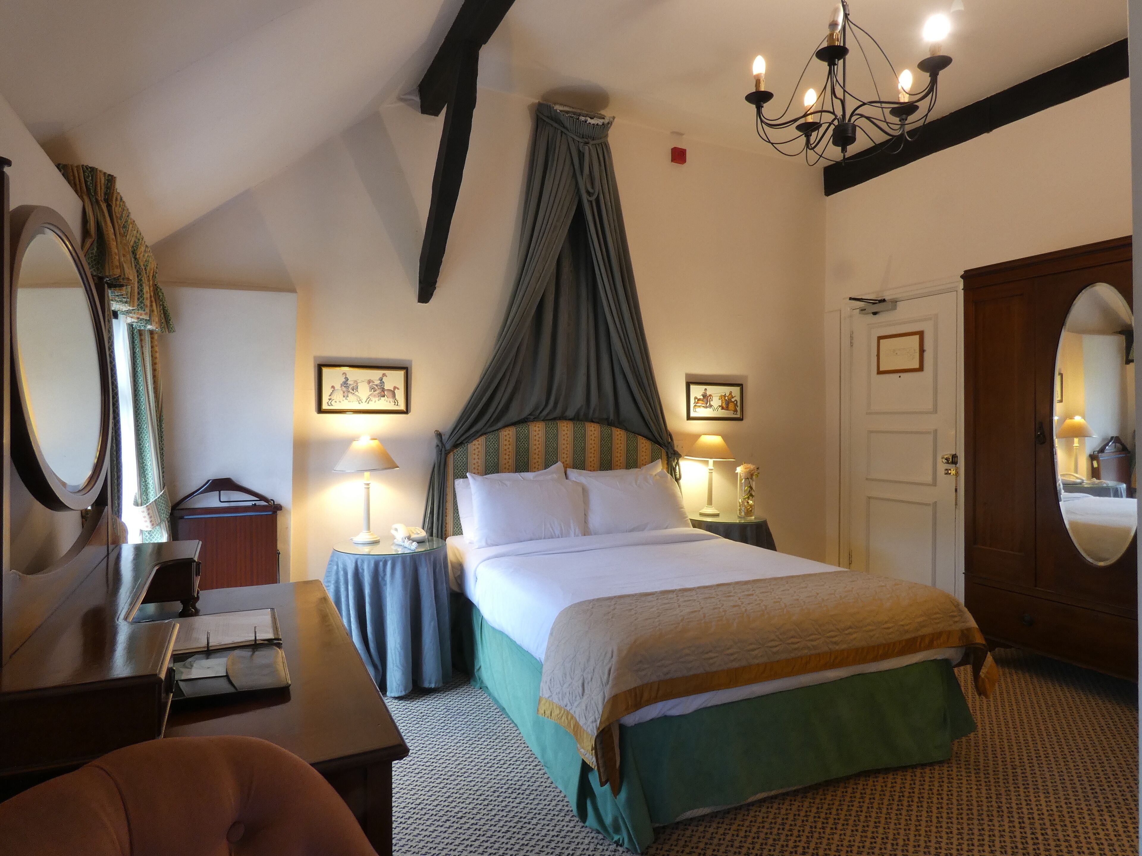 A bedroom with a canopy bed, a large mirror, a desk, and a wardrobe.