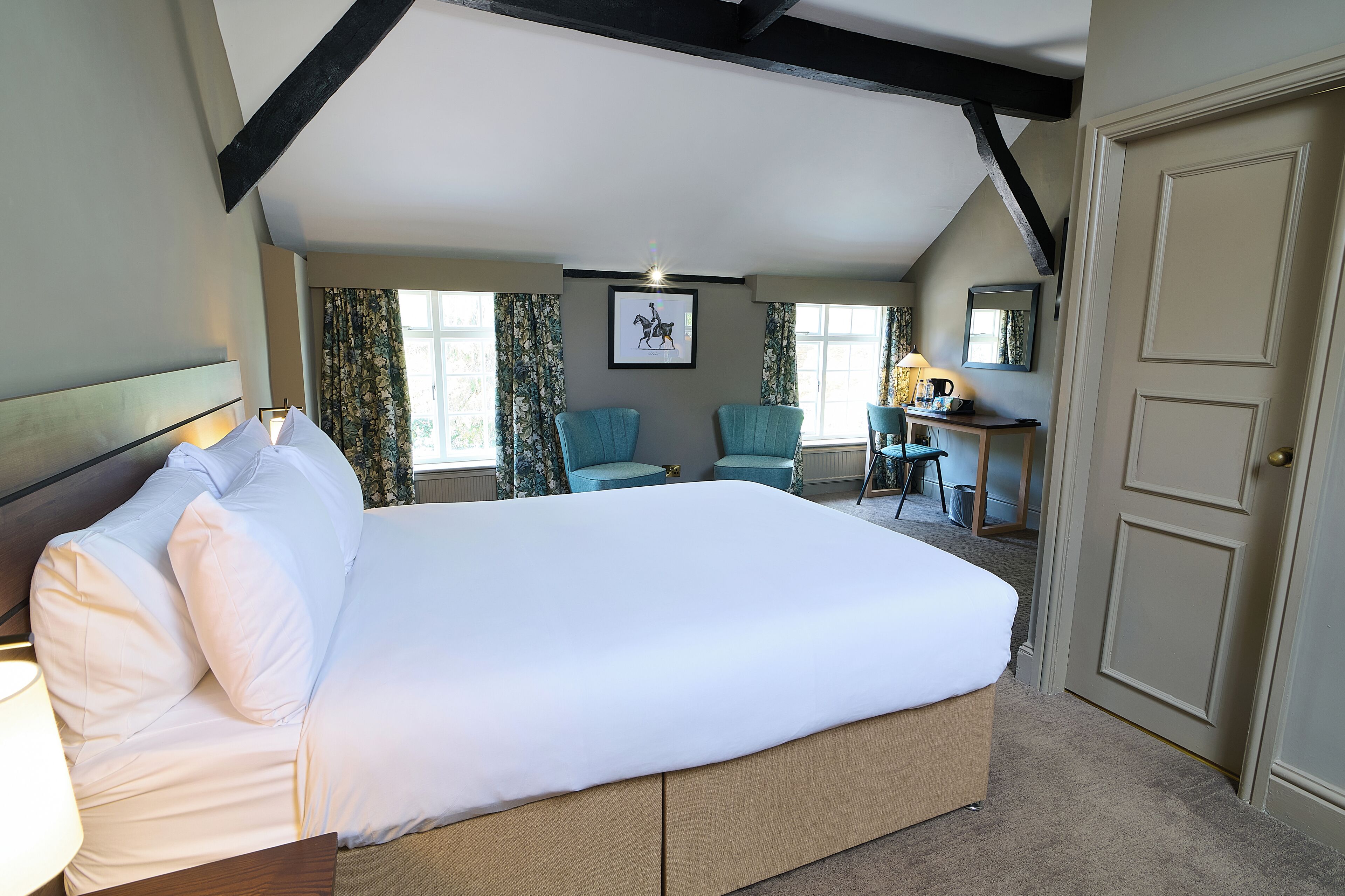 A hotel room with a large bed, a desk, two chairs, and a door.