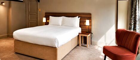 Une chambre d’hôtel avec un grand lit, une table de chevet, une chaise et un miroir.
