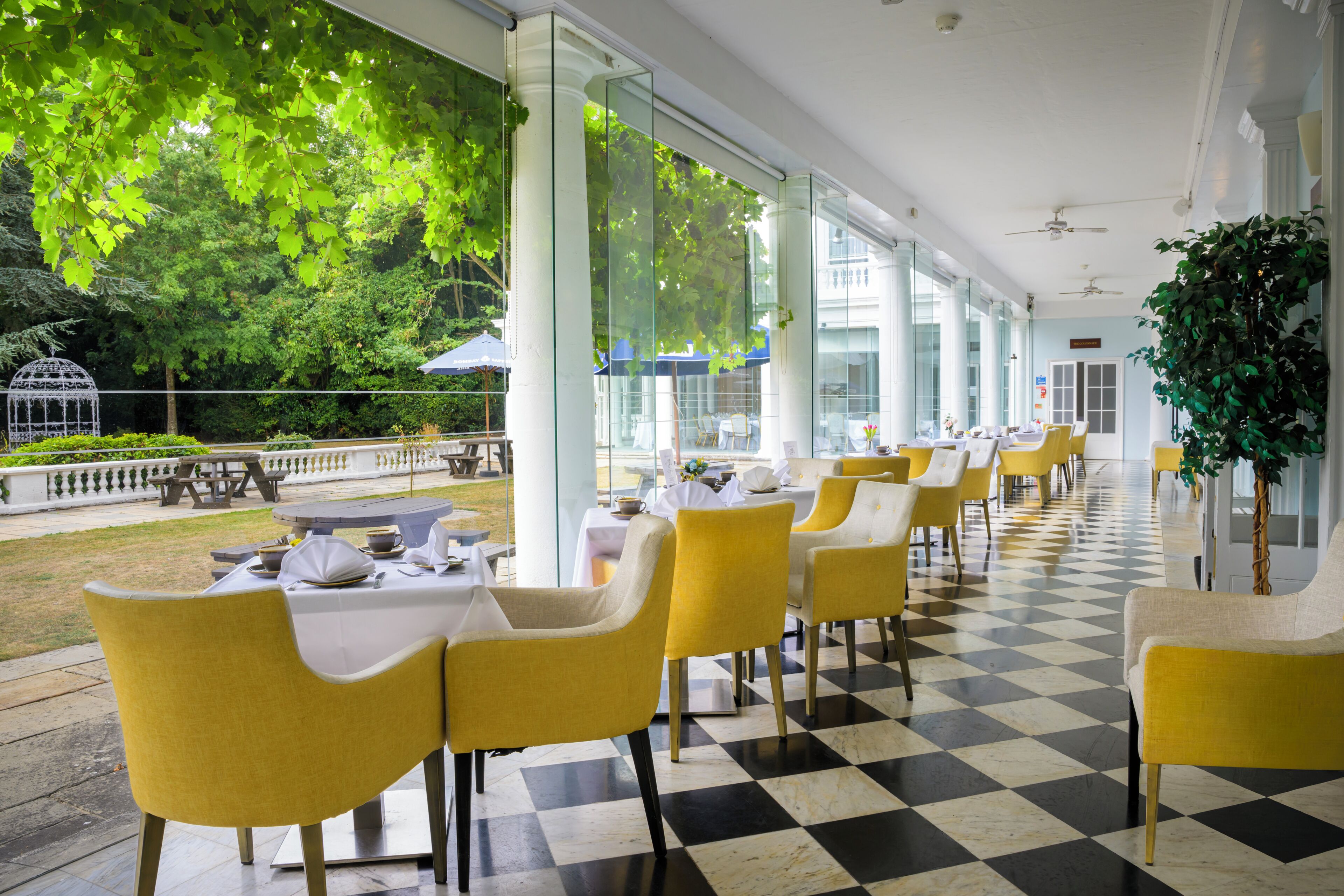 Un restaurante con sillas y mesas amarillas, ventanas amplias y un suelo a cuadros.
