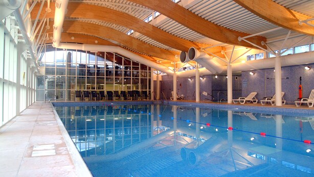 An indoor swimming pool with clear glass walls, wooden beams, and lounge chairs along the poolside. - Manor of Groves Hotel, Golf & Health Club (Sawbridgeworth)