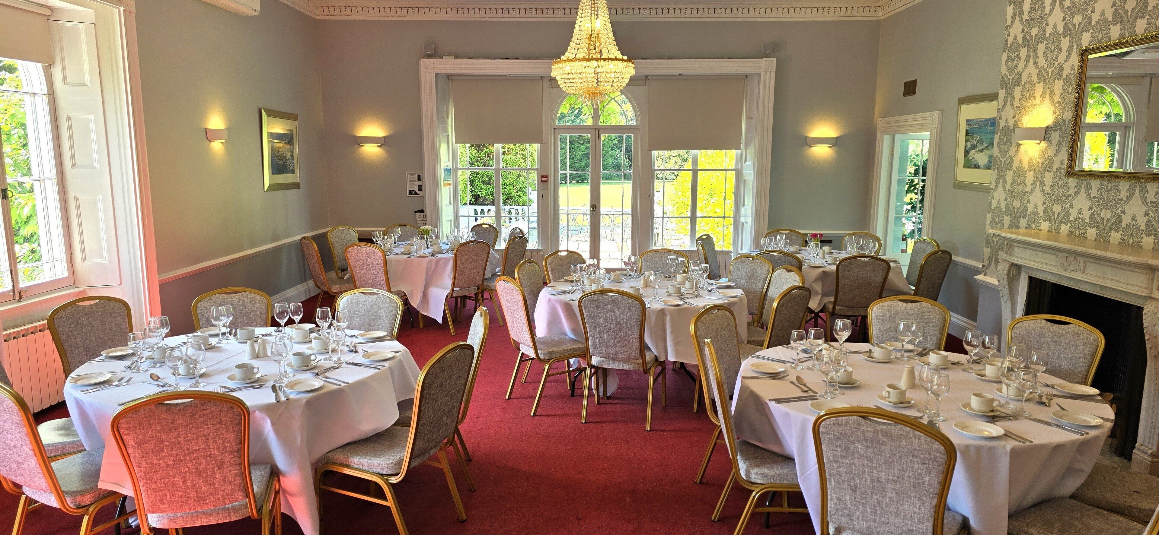 A formal dining room with round tables, gold chairs, and white tablecloths.