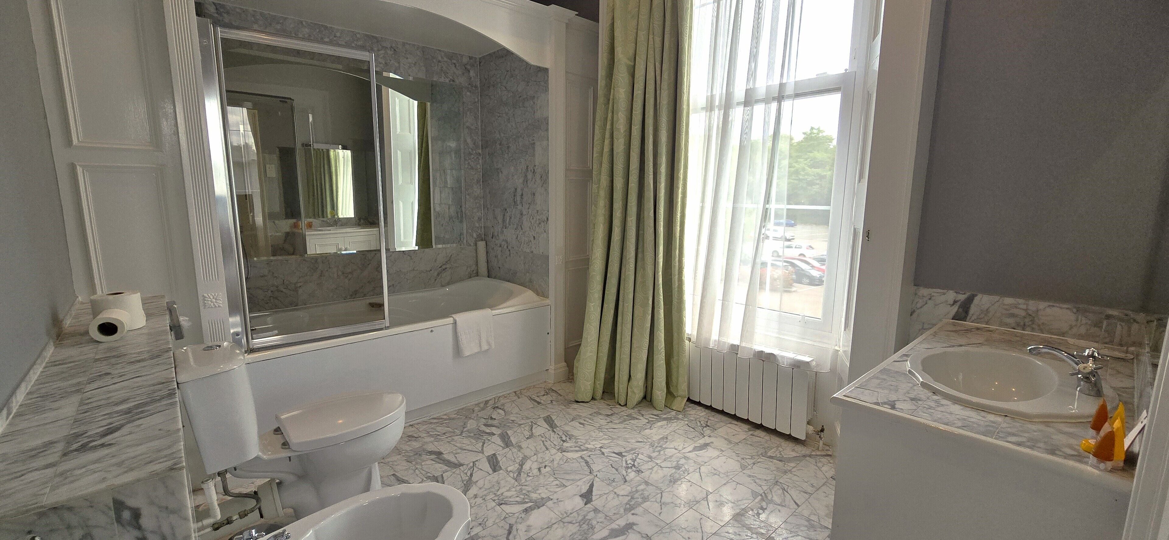 A bathroom with a marble floor, a bathtub, a toilet, a sink, and a large mirror.