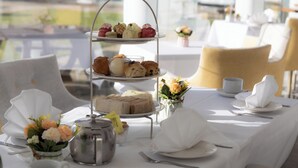 A three-tiered dessert stand with pastries and sandwiches, a white tablecloth, and a vase of flowers. - Manor of Groves Hotel, Golf & Health Club (Sawbridgeworth)