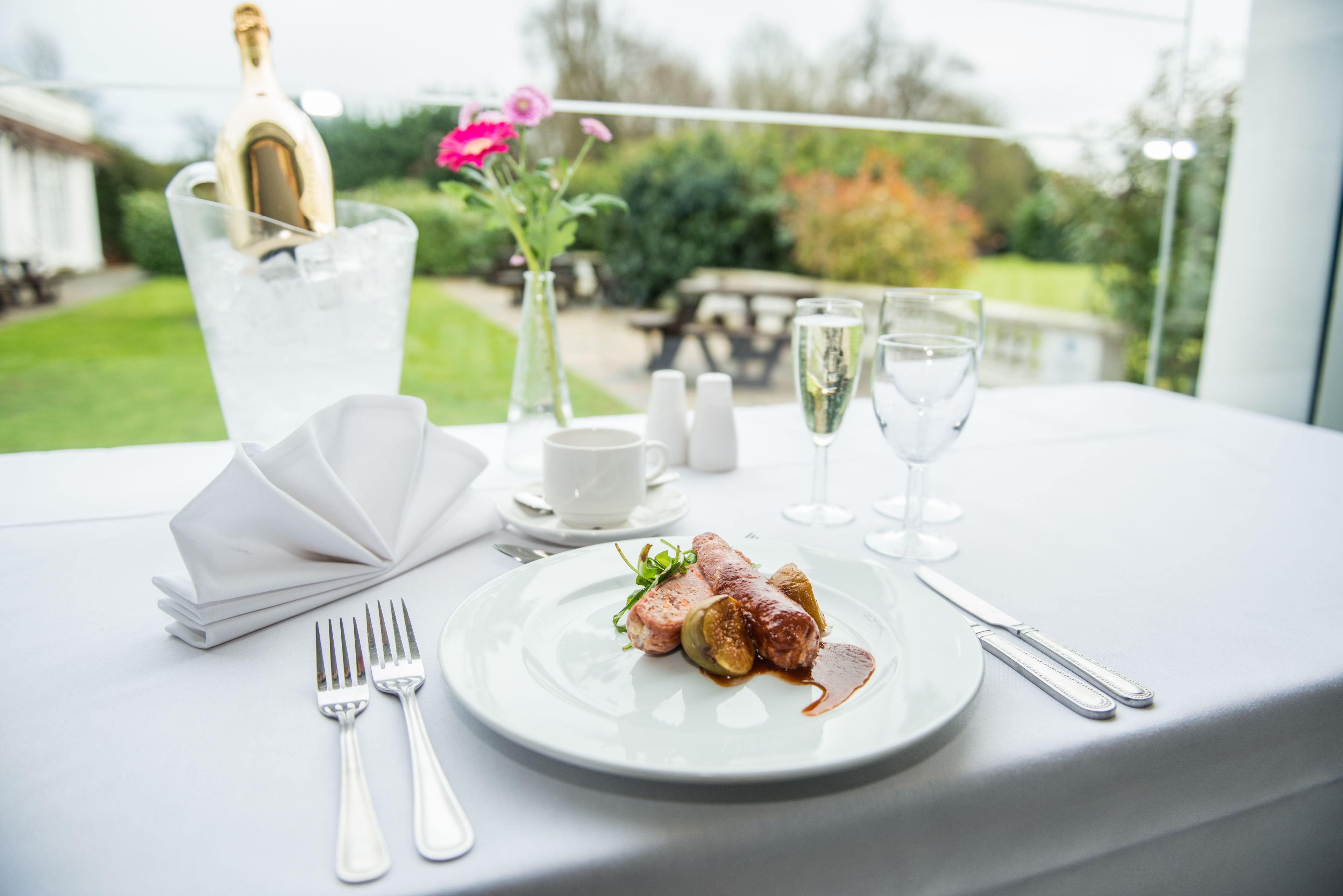 A table set for a meal with a bottle of champagne, a vase with flowers, and a plate of food.