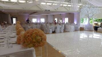 A banquet hall with tables set for a formal event, featuring white tablecloths and floral centerpieces.
