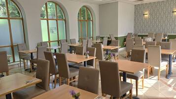 A spacious dining area with multiple tables and chairs, large arched windows, and a patterned wall.