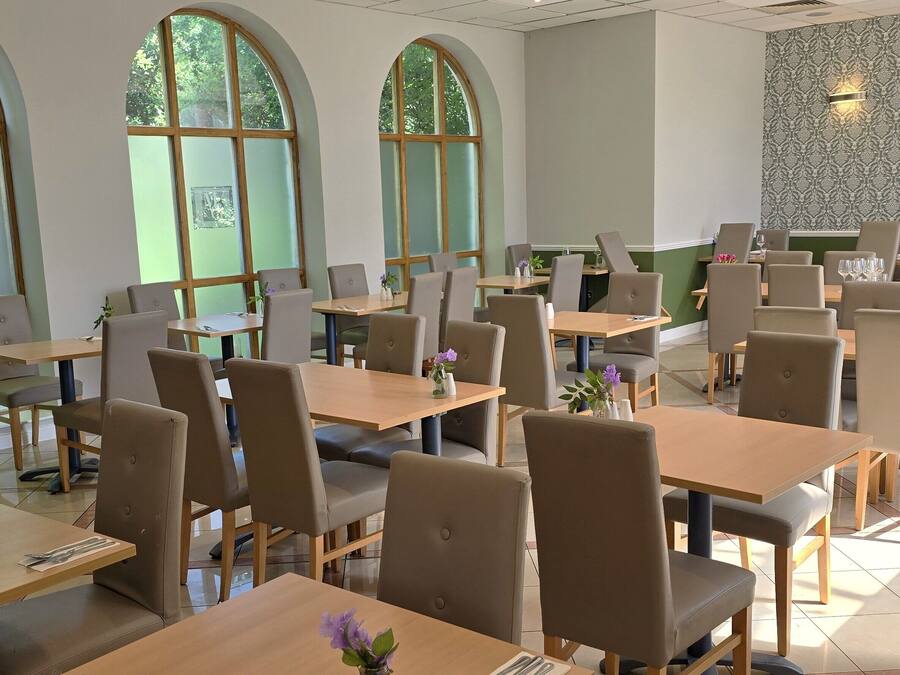 A spacious dining area with multiple tables and chairs, large arched windows, and a patterned wall.