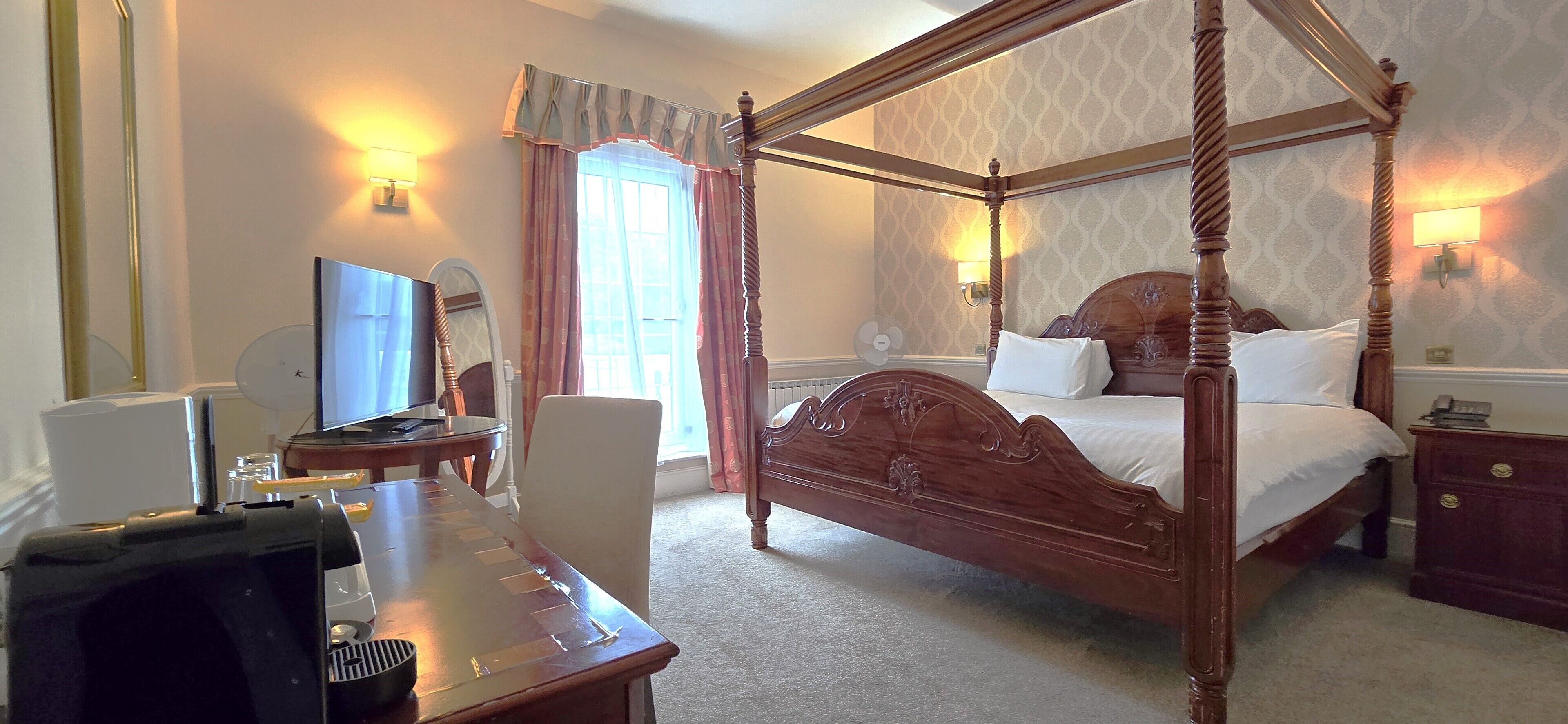 A four-poster bed with a wooden headboard, a desk with a computer, a chair, and a lamp.
