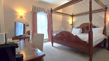 A four-poster bed with a wooden headboard, a desk with a computer, a chair, and a lamp.