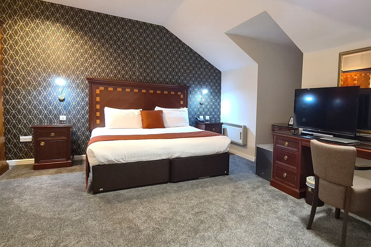 A hotel room with a bed, desk, chair, television, and a mirror.