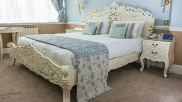 A classic four-poster bed with a blue and white patterned bedspread, a white nightstand with a lamp, and a small table with a book and a phone.