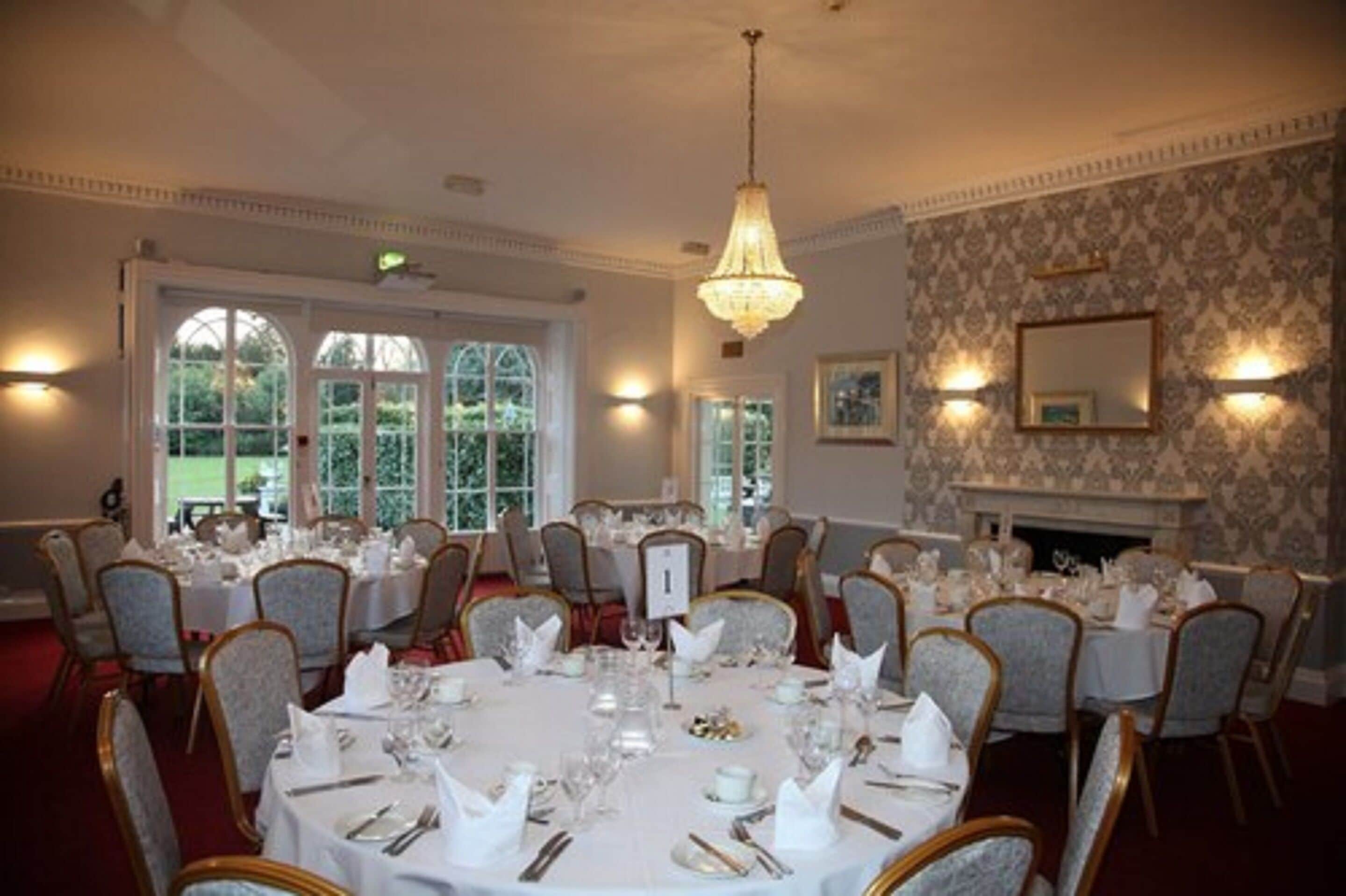 A formal dining room with round tables set for a meal, large windows, and a fireplace.