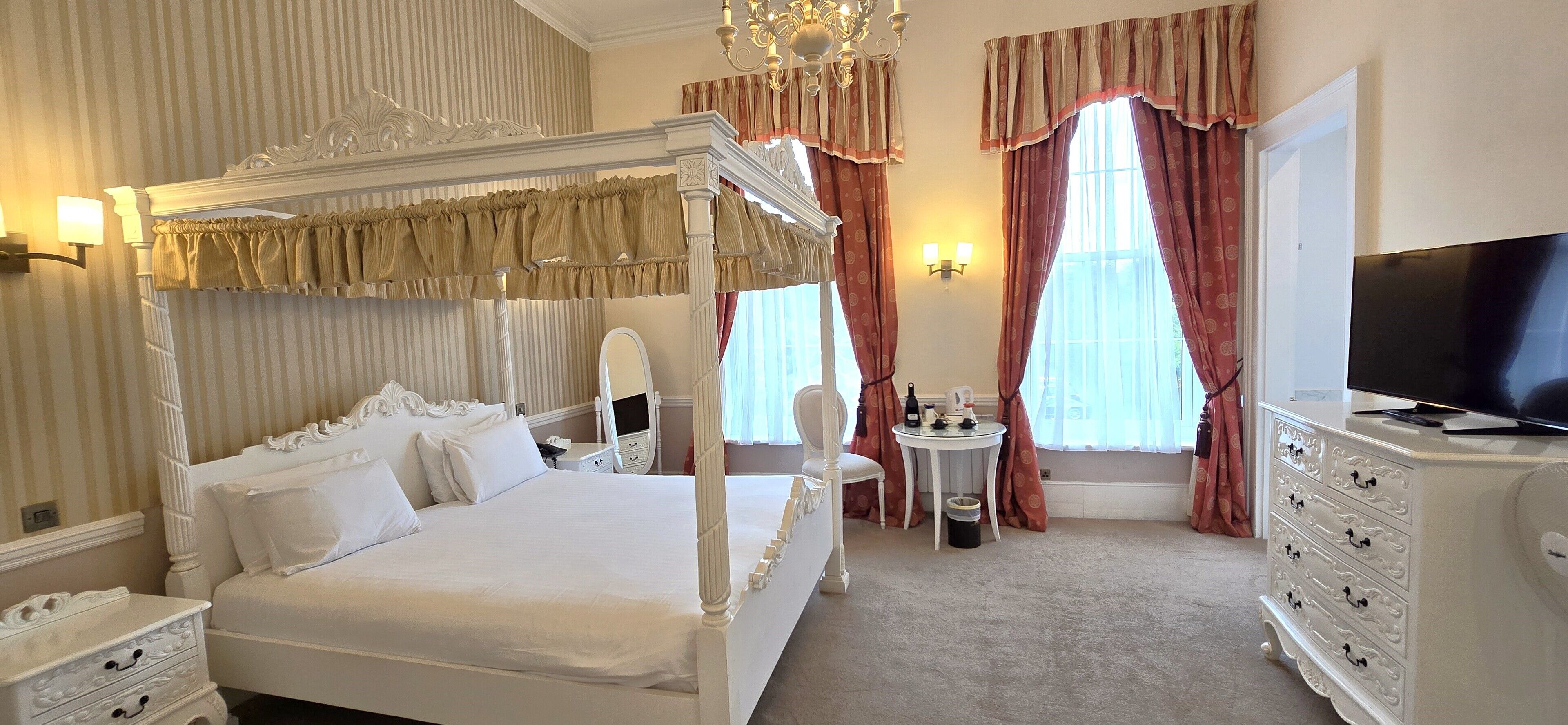 A four-poster bed with a canopy, a television on a dresser, and a small round table with a chair.