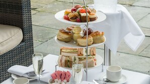 A table set for a tea service with a champagne bottle, sandwiches, and pastries. - Manor of Groves Hotel, Golf & Health Club (Sawbridgeworth)