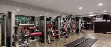 A gym with various exercise machines, a reception desk, and a wooden floor.
