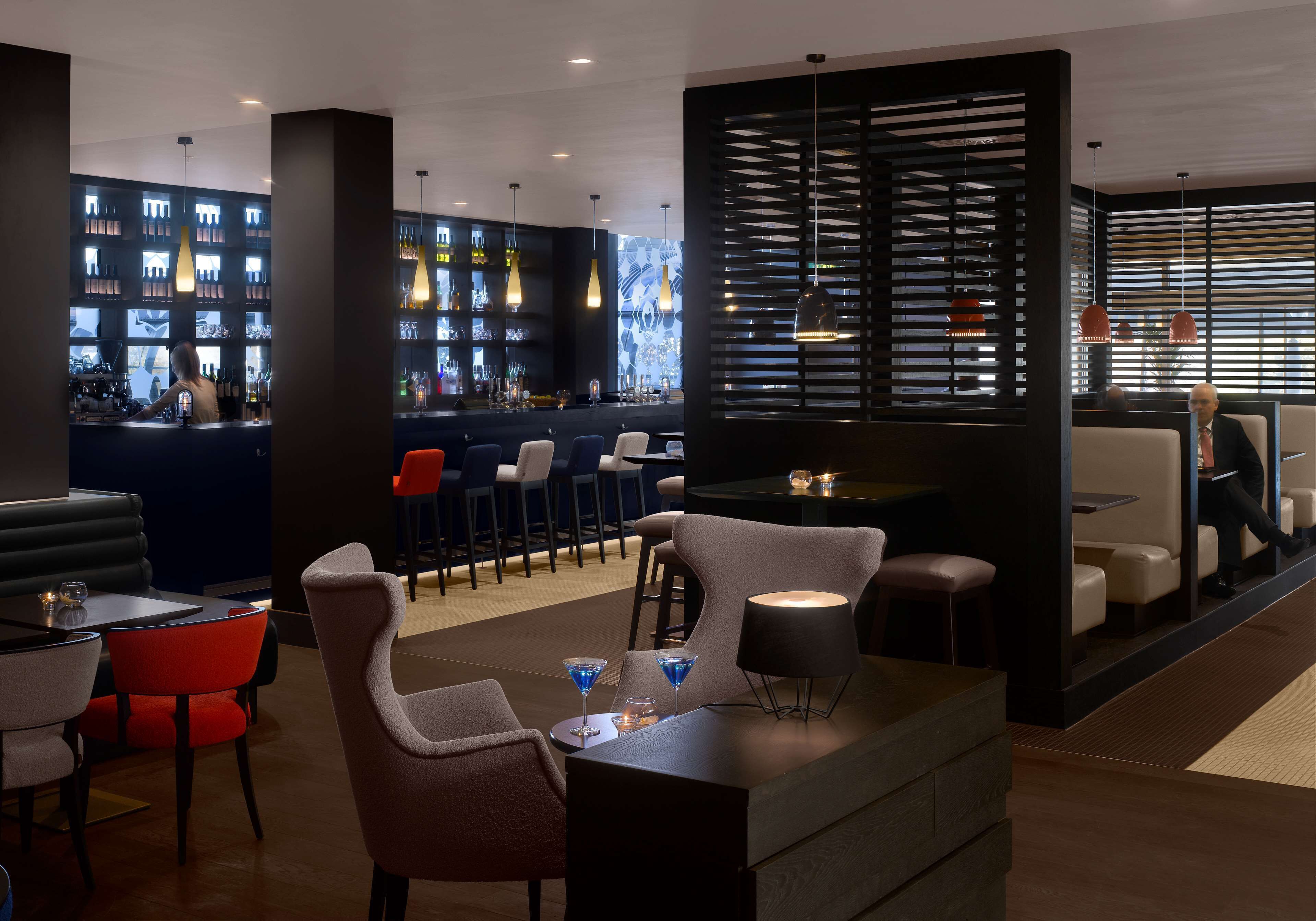 A modern bar area with seating, a bar counter, and shelves with bottles.