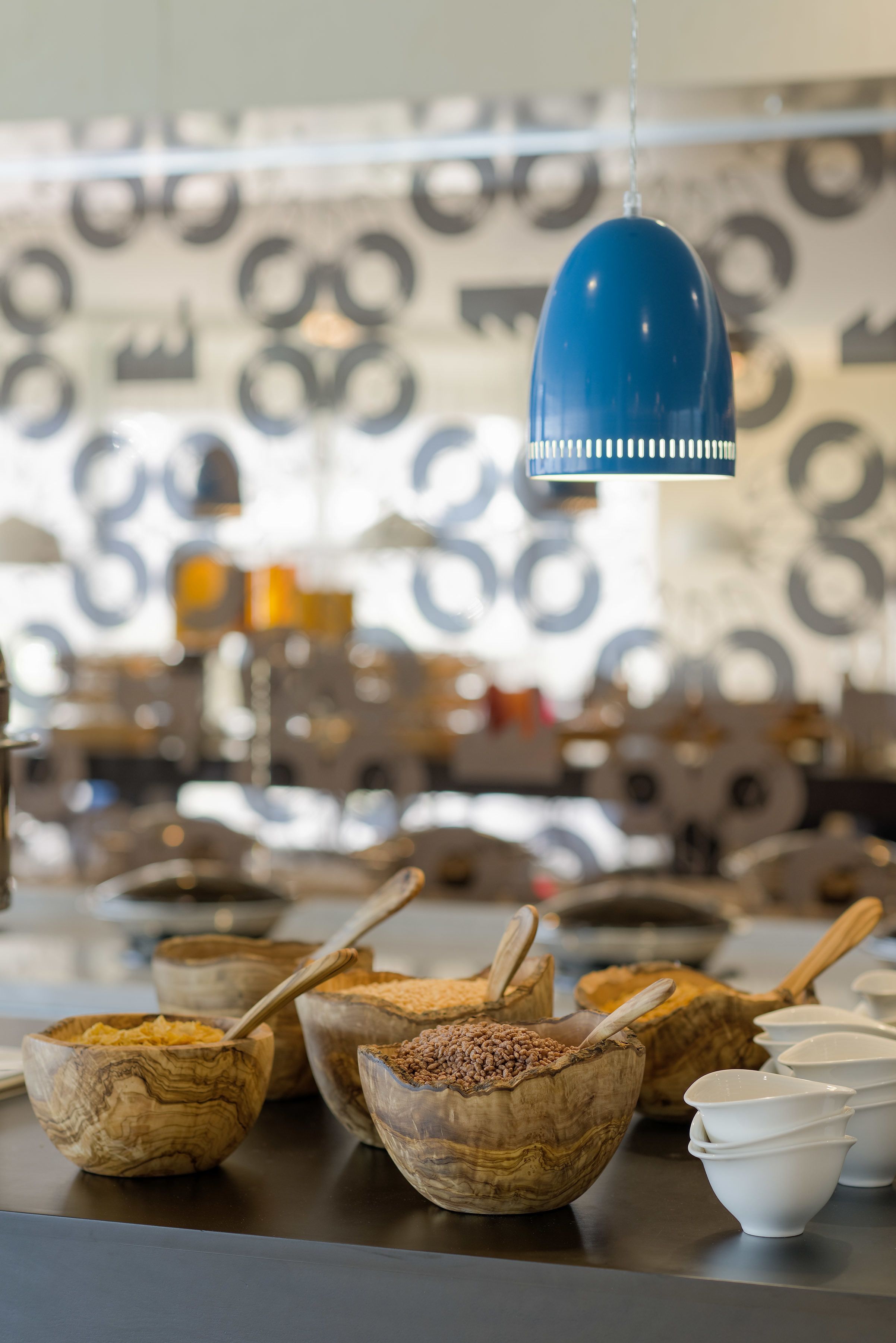Una cocina con cuencos de madera sobre una encimera, una lámpara colgante azul y un papel tapiz estampado al fondo.