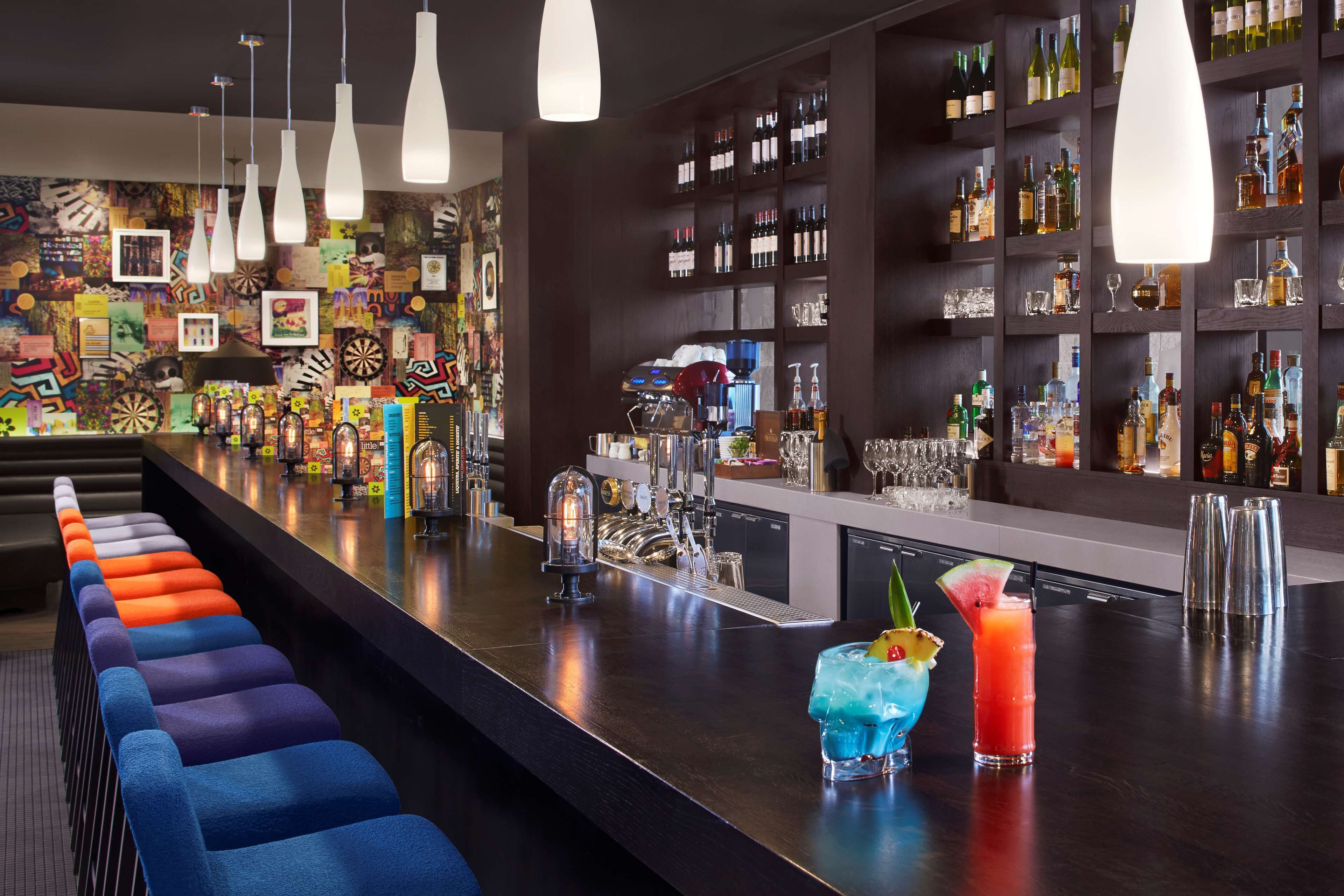 A bar area with a long counter, colorful bar stools, and a variety of bottles and glasses on shelves.
