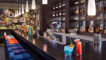 A bar area with a long counter, colorful bar stools, and a variety of bottles and glasses on shelves.