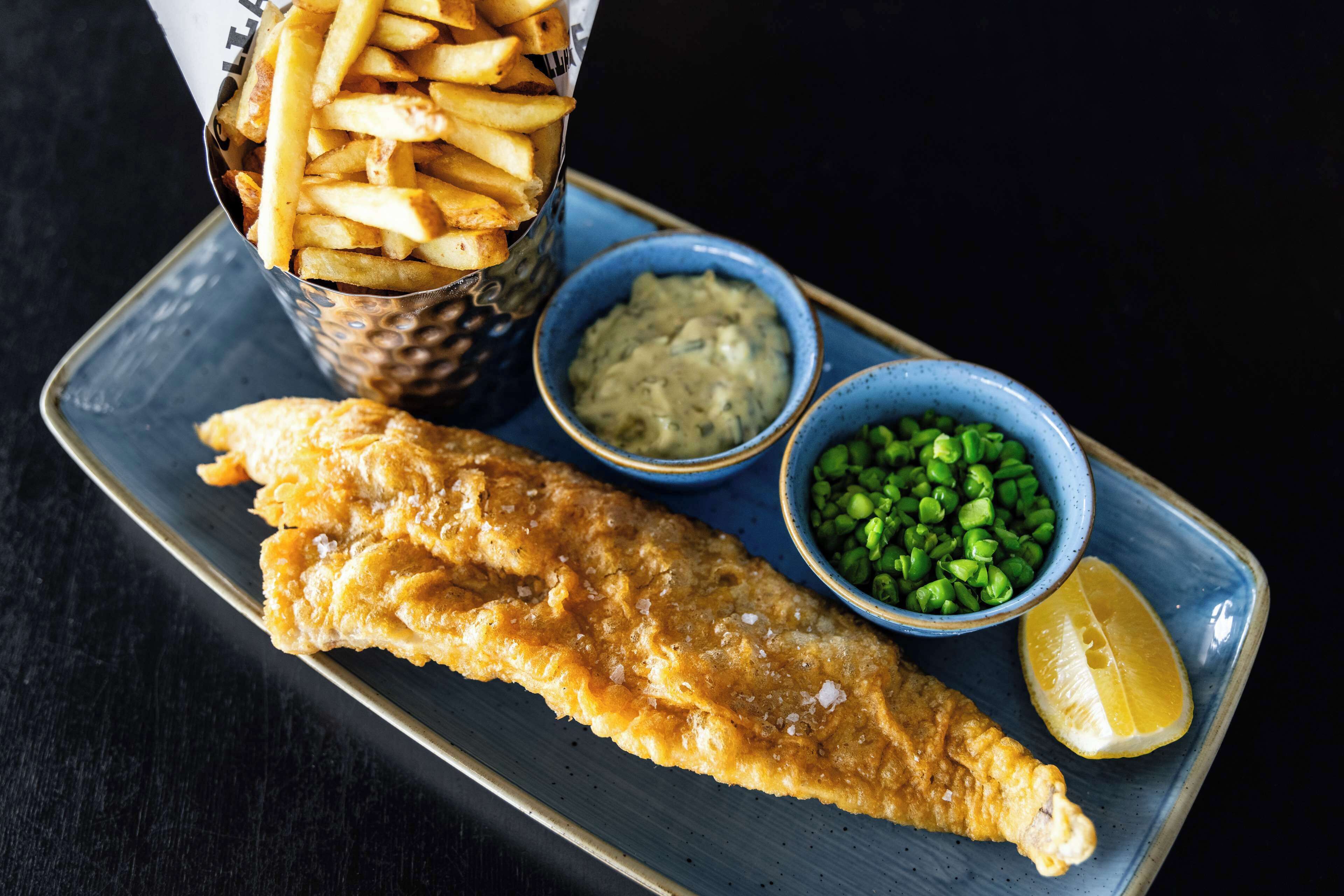 A plate with fish and chips, peas, and a lemon wedge.
