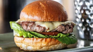 A burger with a toasted bun, lettuce, tomato, and cheese, served on a plate.