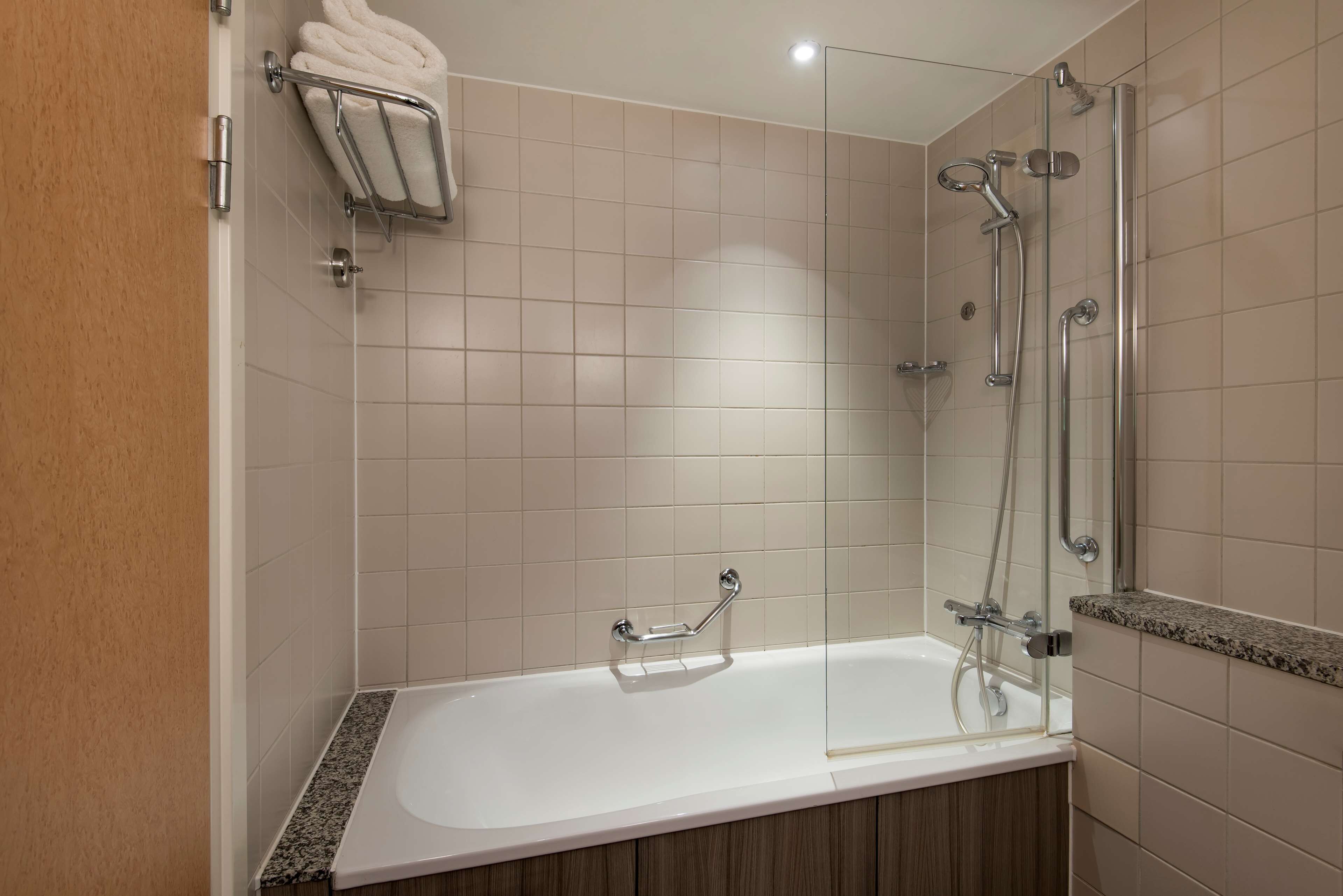A modern bathroom with a glass-enclosed shower, a white bathtub, and a towel rack.